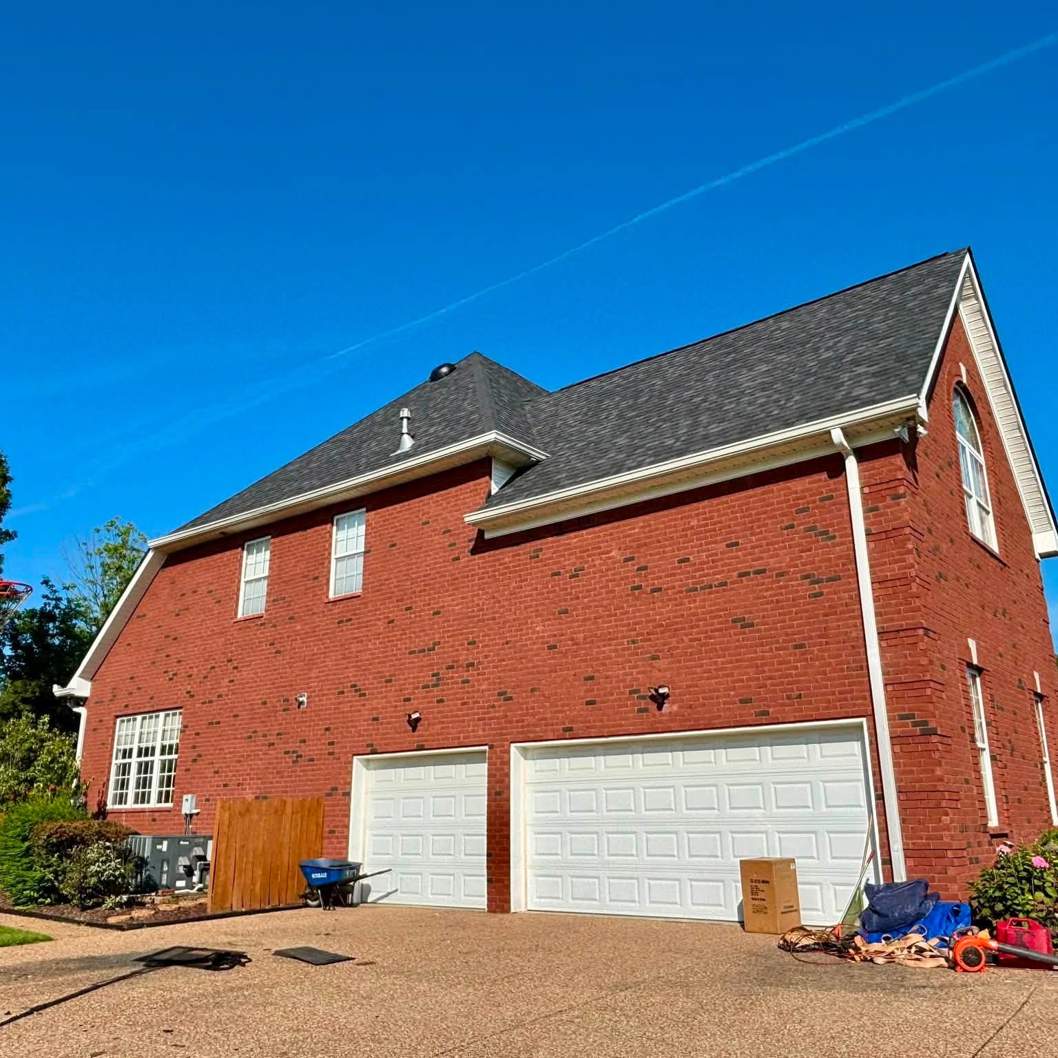 Two-story red brick home with a freshly installed dark shingle roof
