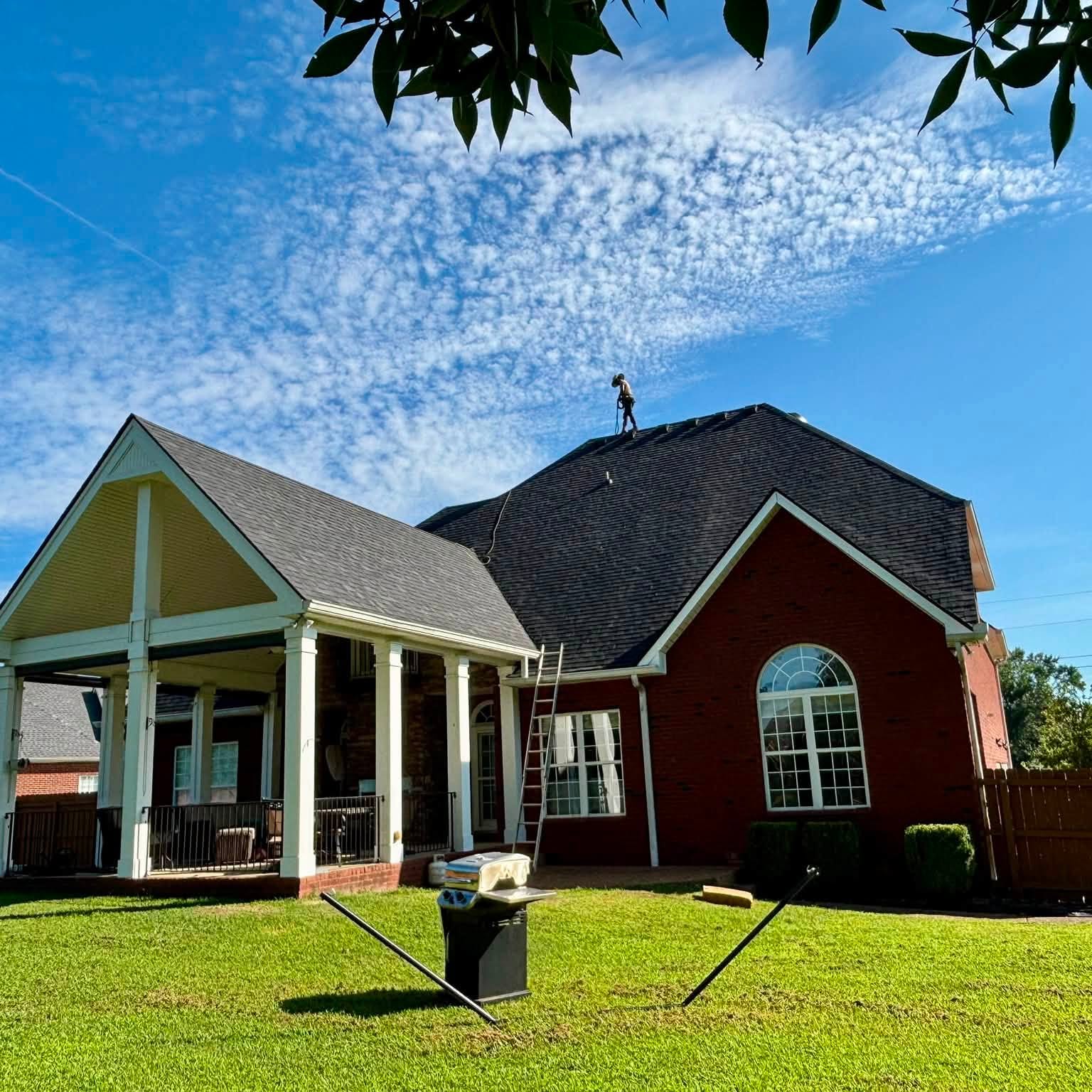 Roofer on the ridge of a home with a covered back porch during a roof replacement