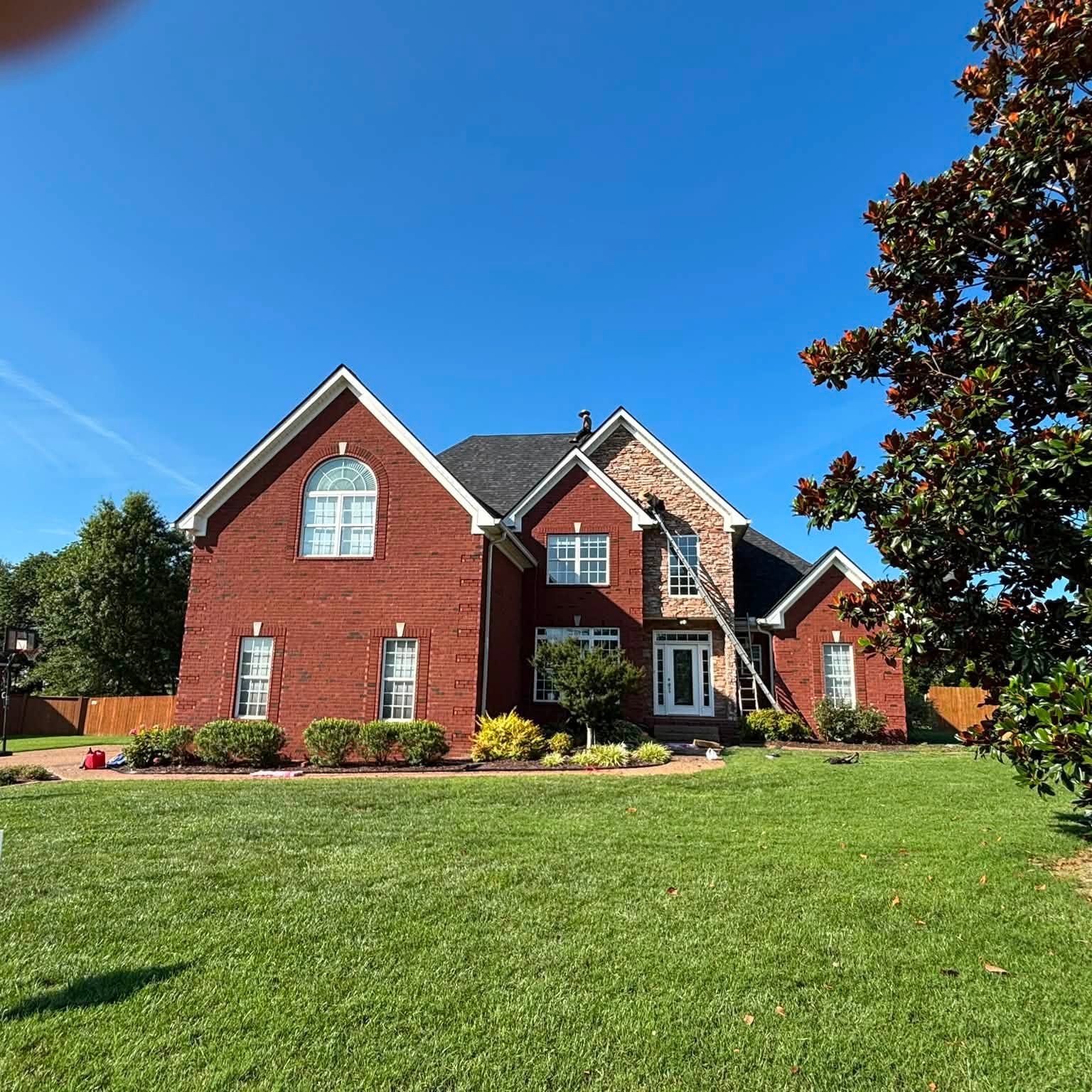 Brick and stone home with ladders up during a roof install